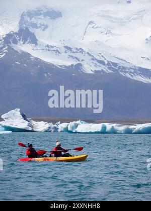 Jokulsarlon, Island - 16. Mai 2024: Das Foto zeigt Menschen beim Kajakfahren im klaren Gletscherwasser, eingerahmt von schneebedeckten Bergen und Eisbergen. Stockfoto