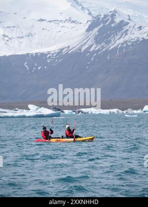 Jokulsarlon, Island - 16. Mai 2024: Das Foto zeigt Menschen beim Kajakfahren im klaren Gletscherwasser, eingerahmt von schneebedeckten Bergen und Eisbergen. Stockfoto