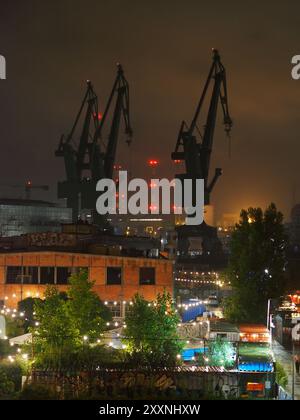 Danzig, Polen - 13. Juli 2024: Nächtliche Stadtlandschaft mit beleuchteten Gebäuden und hoch aufragenden Kränen im Vordergrund, die das geschäftige Treiben der Stadt zeigen Stockfoto