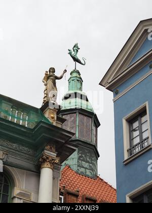 Danzig, Polen - 13. Juli 2024: Eine wunderschöne architektonische Aufnahme, die einen historischen grünen Kupferturm und ein detailliertes Backsteingebäude mit komplizierten St. Stockfoto