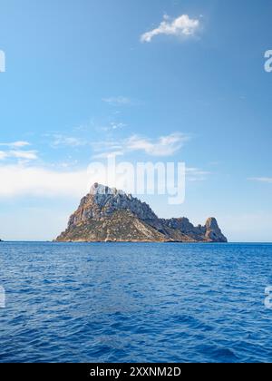 Tagesfoto der Insel es Vedra vor der Küste Ibizas, vom Meer aus aufgenommen, mit blauem Himmel und ein paar Wolken am Horizont Stockfoto