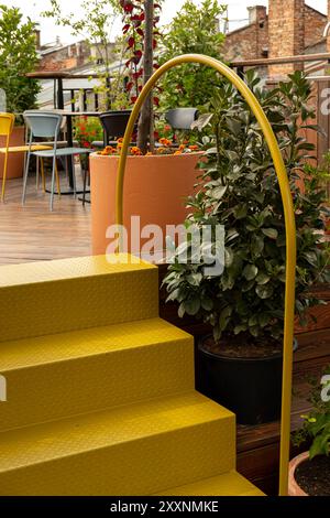 Eine lebhafte Dachterrasse mit gelben Treppen, Topfpflanzen und Sitzgelegenheiten im Freien. Die Szene strahlt eine gemütliche, urbane Atmosphäre aus, die perfekt zum Entspannen ist Stockfoto