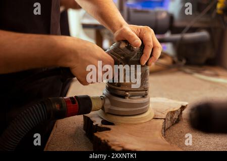 Handwerker im Studio, der sich für diy-Hobby einsetzt und Schwingschleifer mit feinem Schleifpapier auf Holz verwendet, um ein glattes Finish zu erzielen. Kreative Person in der Tischlerei verwendet Winkelschleifer, um Holzobjekte zu kreieren Stockfoto