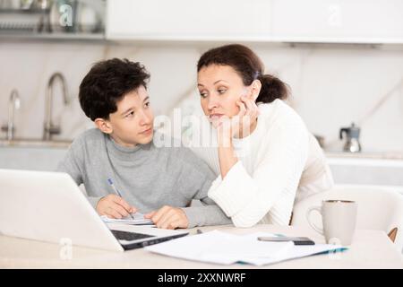 Mutter hilft ihrem Sohn im Teenageralter, Schularbeit zu leisten, Probleme gemeinsam zu lösen und Antworten zu finden Stockfoto