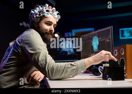 Mann, der ein EEG-Headset trägt und eine Diskette in einen PC mit Software einsteckt, der KI in ein empfindliches Wesen verwandelt und den Schöpfer anregt. Der Ingenieur legt die Kartusche in den Computer und weckt damit freundliche künstliche Intelligenz Stockfoto