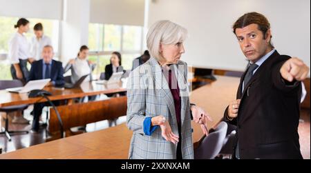 Ein wütender Geschäftsmann, der eine traurige Seniorin entlassen Stockfoto