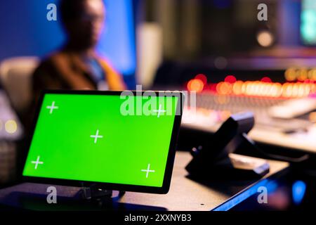 afroamerikanischer Audiotechniker, der Titel neben einem isolierten Display auf einem Tablet bearbeitet und auf der Schalttafelplatine des Kontrollraums arbeitet. Musiktechniker drückt Fader und Tasten im Postproduktionsstudio. Stockfoto