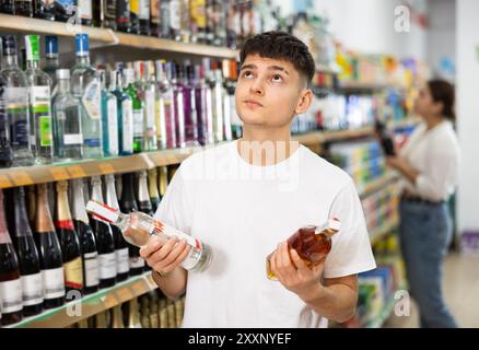 Interessierter junger Kerl, der alkoholische Getränke im Laden auswählt Stockfoto