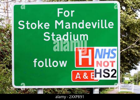 A413 Stoke Mandeville Straßenschild für Stoke Mandeville Hospital und Stadium mit Anti HS2 Schild angebracht. Auf dem Anti-HS2-Schild steht NHS, nicht HS2. Wer auch immer das NHS-NICHT-HS2-Zeichen herstellte, glaubte wahrscheinlich, dass das Geld, das für HS2 ausgegeben wurde, zur Unterstützung des NHS verwendet werden sollte. Ein paar Kilometer entfernt am Stadtrand von Aylesbury beginnt die zweite Woche der HS2-Schließung der A418, was zu extremen Groll bei den Anwohnern, Verkehrsverzögerungen und Umleitungen sowie Geschäftsverlusten vor Ort führt. Quelle: Stephen Bell/Alamy Stockfoto