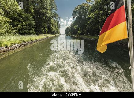 Antriebswelle eines Bootes, das durch einen Kanal fährt, mit einer schwenkenden deutschen Flagge Stockfoto