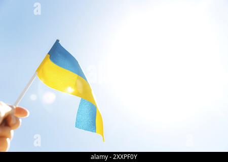 Menschliche Hand mit großer zweifarbiger gelbblauer ukrainischer Staatsflagge, nationales Symbol flatternd, winkend im Wind gegen den blauen Himmel an sonnigen Tagen. Ukraine I Stockfoto