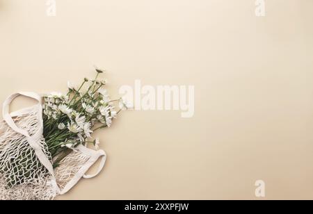 Umweltfreundliches Sommerkonzept auf beigefarbenem Hintergrund mit ECO-Einkaufstasche und weißen Kamillenblüten innen. Stockfoto