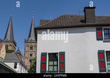Blick auf ein Gebäude mit grünen und roten Fensterläden, im Hintergrund zwei Kirchtürme unter klarem blauem Himmel, Xanten, Niederrhein, Nordrhein-Westfalen Stockfoto