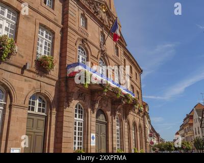 Historisches Rathaus mit französischer Flagge und Blumen auf dem Balkon unter klarem blauem Himmel, Weissenburg, Elsass, Frankreich, Europa Stockfoto