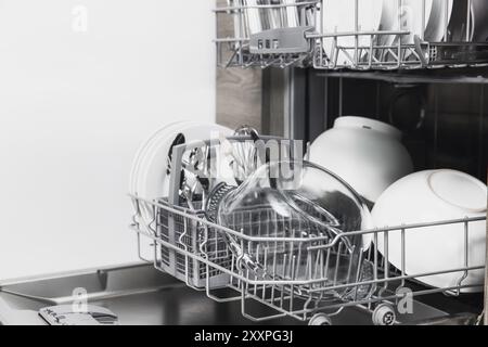 Vorderansicht der offenen automatischen Edelstahl-Einbaumaschine mit vollständig integrierter Steuerung der oberen Spülmaschine mit sauberen Utensilien, Besteck, Gläsern und DIS Stockfoto