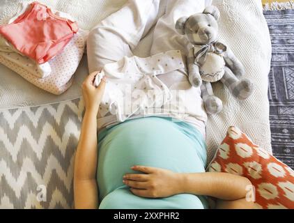 Schwangere Frau ist die Verpackung Baby Kleidung für das Krankenhaus in der Ansicht von oben mit der Mutterschaft Stockfoto