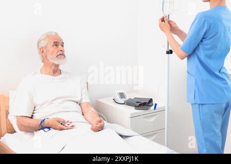 Seniorenmann mit Notruftaste und Krankenschwester Einstellung IV Tropf im Krankenhaus, Nahaufnahme Stockfoto