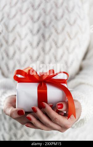 Der Frau mit roten Hände Maniküre, die kleinen weißen Geschenkbox mit roter Schleife Stockfoto