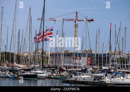 Barcelona, Spanien. August 2024. Die Flagge der britischen Mannschaft winkt im Hafen von Barcelona zwischen Masten und Booten. Das letzte Vorrennen des America's Cup fand statt. Viele Zuschauer verfolgten das Rennen aus dem Race Village in Port de la Fusta, wo auch eine große Auswahl an Gastronomie angeboten wird. Quelle: SOPA Images Limited/Alamy Live News Stockfoto