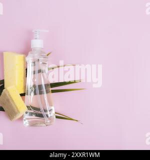 Flache Lage mit grünem Palmblatt, Seifentropfer, Geschirrspülmittel, Geschirrseife, Waschlappen auf pastellrosa und gelbem Hintergrund. Stockfoto