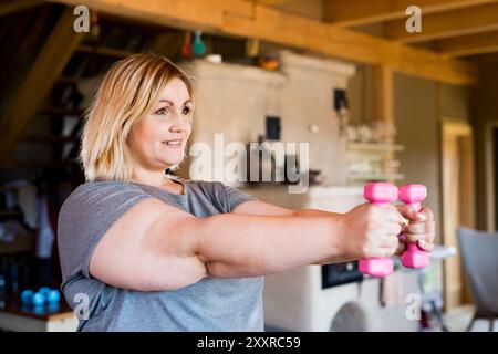 Übergewichtige Frau, die zu Hause trainiert, mit Kurzhanteln. Workout im Wohnzimmer. Stockfoto