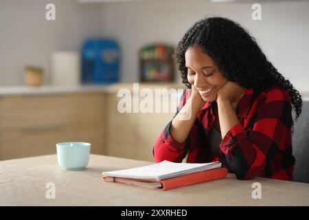 Glücklicher schwarzer Schüler, der in der Küche lernt und Notizen liest Stockfoto