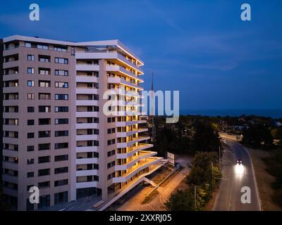 Luftdrohnenaufnahme einer modernen Gebäudefassade, beleuchtet von schlanker LED-Beleuchtung bei Dämmerung, die den Kontrast zwischen der Skyline der Stadt und einfängt Stockfoto