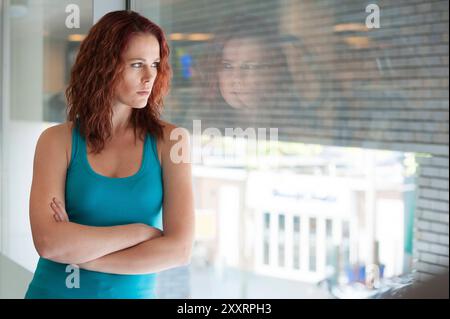 Porträt Junge Aduld Frau, die das Fitnessstudio besucht Porträt junge Erwachsene, rothaarige Frau, die sich während einer Pause von ihrem Fitnessprogramm gegen das Fenster des Fitnessstudios lehnt. Tilburg, Niederlande. MRYES Tilburg Achmea Health Centre Noord-Brabant Nederland Copyright: XGuidoxKoppesxPhotox Stockfoto
