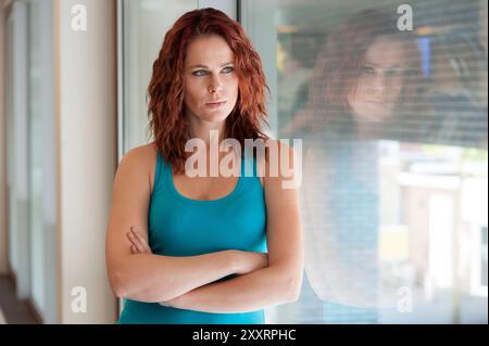 Porträt Junge Aduld Frau, die das Fitnessstudio besucht Porträt junge Erwachsene, rothaarige Frau, die sich während einer Pause von ihrem Fitnessprogramm gegen das Fenster des Fitnessstudios lehnt. Tilburg, Niederlande. MRYES Tilburg Achmea Health Centre Noord-Brabant Nederland Copyright: XGuidoxKoppesxPhotox Stockfoto