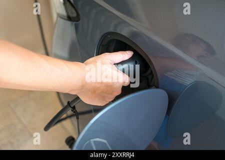 Mann, der sein Elektroauto auflädt. Nahaufnahme des Einsteckens des elektrischen Steckverbinders am Fahrzeug. Stockfoto