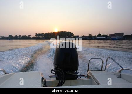 Rückansicht eines Schnellbootes, das die Küste am Morgen verlässt, während der Sonnenaufgang die Berge und die Sonne im Hintergrund sind. Stockfoto