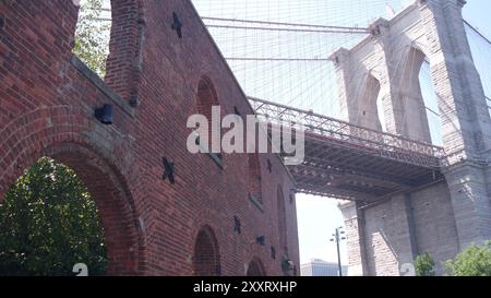 New York City Brooklyn Bridge von Dumbo. Rote Backsteinmauer, altes historisches Tabaklager, Markt und Theater. Flachwinkelansicht. Bogenfenster unter dem berühmten Wahrzeichen. Reisen Sie durch die Architektur der USA Stockfoto