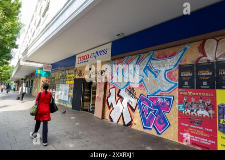 Notting Hill, London, Großbritannien. August 2024. Europas größtes Straßenfest findet später in den Straßen von Notting Hill statt. Exotische Tänzer und Musikgruppen im jamaikanischen Stil ziehen durch die Straßen, während Speisen und Unterhaltung in der Gegend zur Veranstaltung beitragen. Die Grand Parade findet am Montag der Bank als Höhepunkt des dreitägigen Festivals statt, das 1966 begann. Die Teilnehmer versammeln sich in der Nähe und bereiten ihre farbenfrohen Kostüme vor, mit Sicherheitspolizisten und Graffiti-bedeckten Schutzschildern. An Bord des Tesco Stores Stockfoto