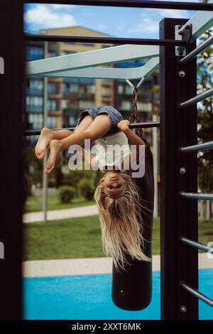 Das junge Mädchen hängt kopfüber auf dem Spielplatz. Stockfoto