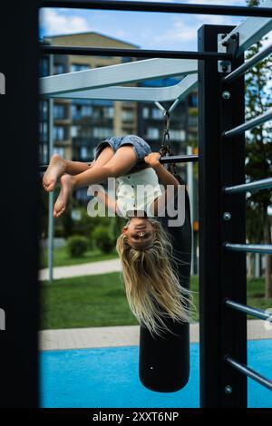 Das junge Mädchen hängt kopfüber auf dem Spielplatz. Stockfoto