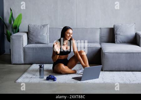 Personal Trainer, der Videoanrufe führt, während er sich auf dem Boden vor dem Laptop auflegt. Stockfoto