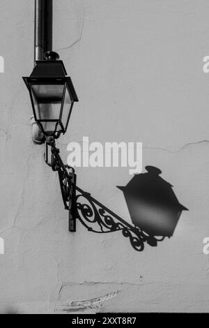 Schmiedeeiserne Laterne mit ihrem Schatten auf einer Straßenmauer, Colmar, Elsass, Frankreich. Schwarzweißbild. Beleuchtung. Straßenlaterne. Schwarzweißbild. Stockfoto