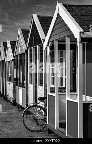 Fahrrad versteckt sich an einem Sommertag zwischen Strandhütten an der Küste von Southwold, Suffolk. Muster. Konzept. Abstrakt. Schwarzweißbild. Stockfoto