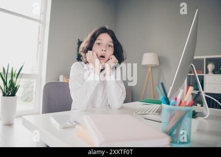 Foto eines intelligenten, süßen kleinen Jungen, der ein weißes Hemd trägt und von Zuhause aus lernt Stockfoto