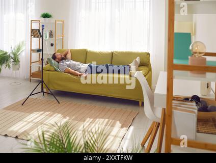 Glücklicher, entspannter Mann, der eine intravenöse Vitaminspritze auf der Couch zu Hause bekommt Stockfoto