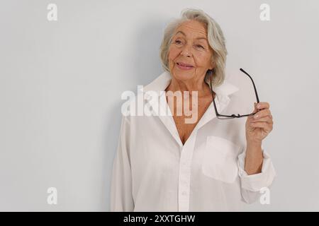 Eine anmutige ältere Frau in einem stilvollen weißen Hemd strahlt Selbstvertrauen und Eleganz aus Stockfoto