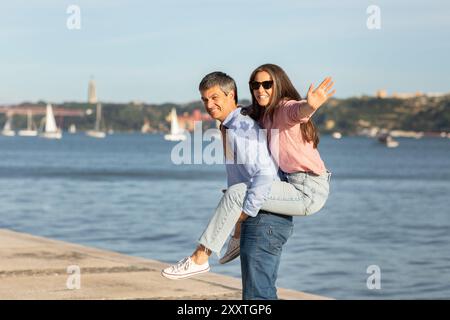 Glückliches Paar, das einen verspielten Moment am Wasser an sonnigen Tagen genießt Stockfoto