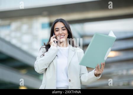 Junger Profi telefoniert draußen, während er einen Dokumentenordner hält Stockfoto