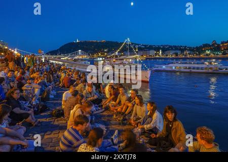 Ungarn, Budapest, nächtliche Sicht auf eine Gruppe von Menschen, die sich am Donauufer neben Kreuzfahrtschiffen, die auf der Donau und mit der E vertäut sind Stockfoto