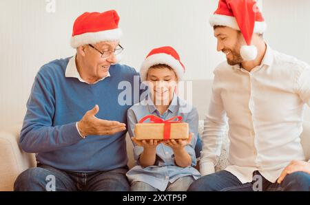 Junge empfangen Weihnachtsgeschenk von Papa und Opa sitzend Indoor Stockfoto