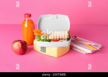 Lunchboxen mit Snacks, Flasche Saft, Wecker und Schreibwaren auf rosa Hintergrund Stockfoto