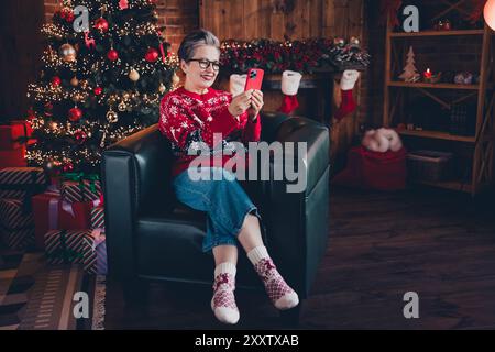 Foto der niedlichen positiven Frau tragen roten Druck Weihnachtspullover Brille bekommen weihnachten sms instagram twitter Telegramm facebook Indoor Apartment Zimmer Stockfoto