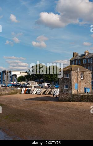 EDINBURGH - 28. JULI 2024: Farbenfrohe Boote stehen neben einem malerischen Steingebäude des Fisherrow Harbour Office mit Bäumen und blauem Himmel. Stockfoto