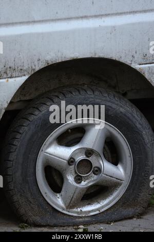 Dreckiges Autorad mit einem Platten Reifen und Anzeichen von Stilllegung. Vertikales Foto, Kopierraum. Stockfoto