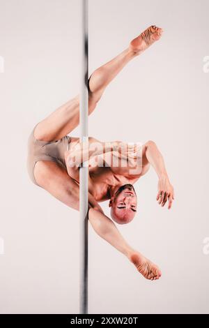 Aufnahme in voller Länge eines muskulösen erwachsenen Mannes, der anmutig die Stange hält und Akrobatik vorführt, die Stärke und Flexibilität im Studio demonstriert Stockfoto